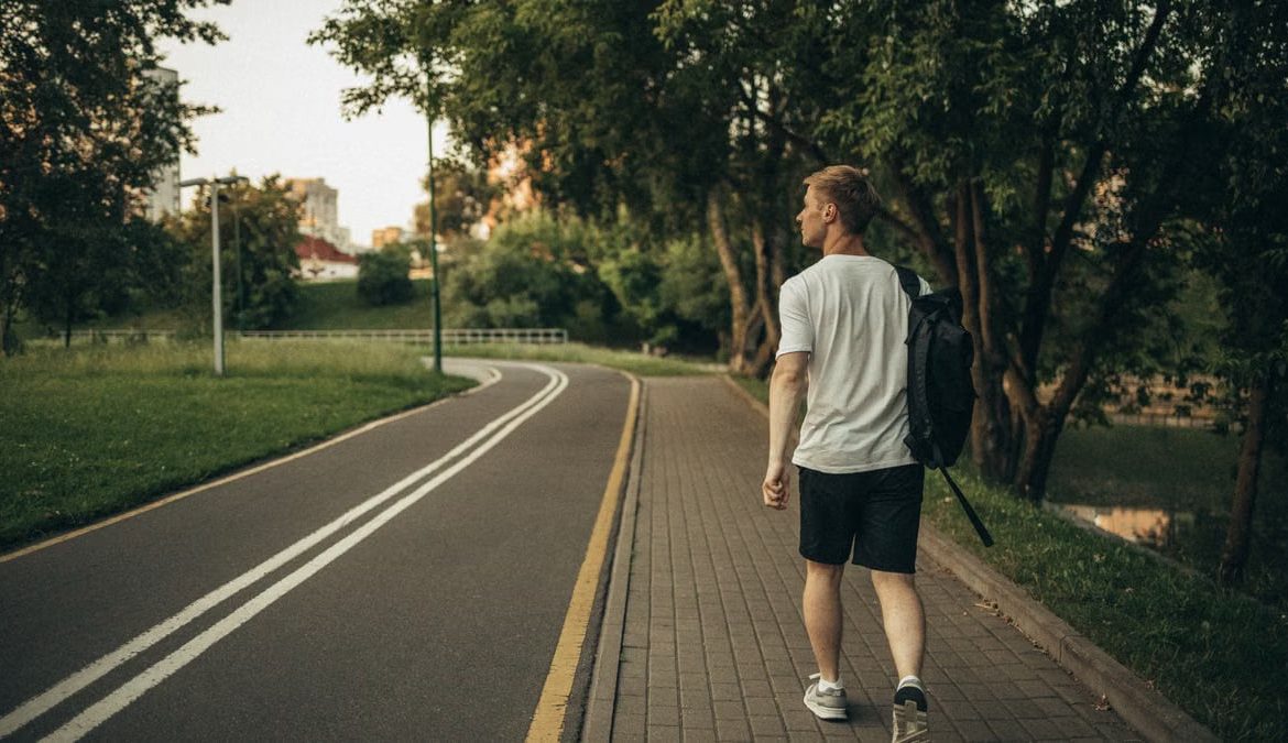 A man walks through a peaceful park on a paved path surrounded by lush greenery.